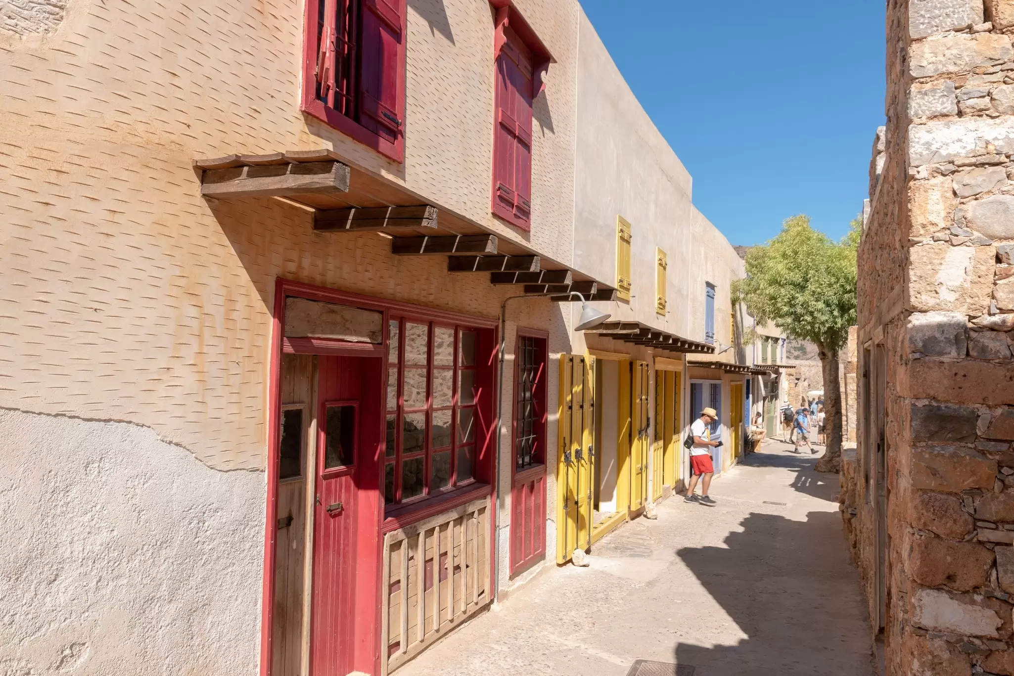 Tourists walk down a narrow street and in between old buildings on the island of Spinalonga, Crete, Greece.