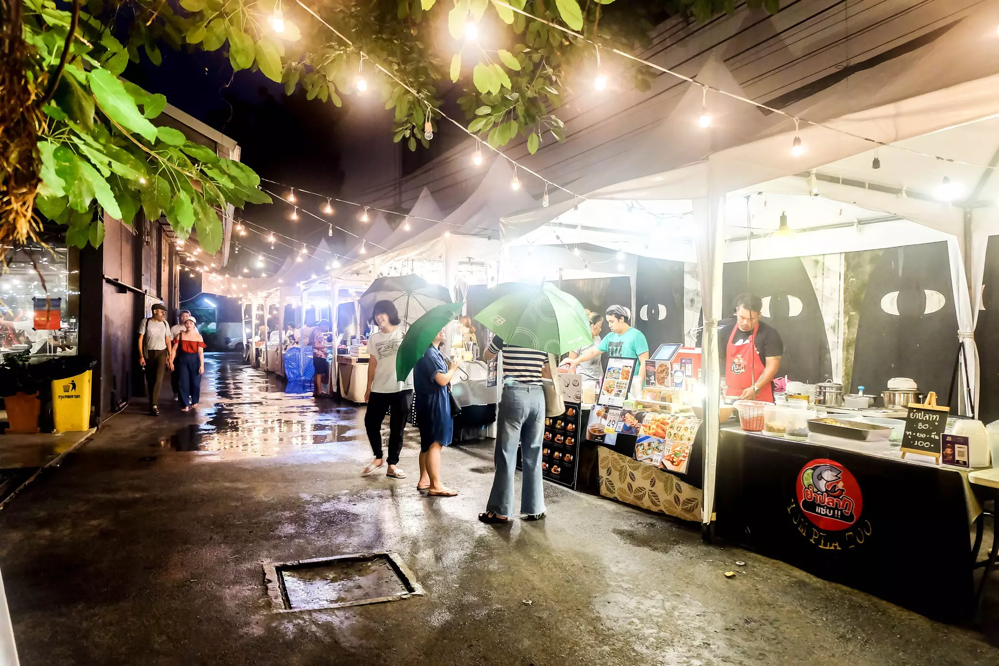 A group of people with umbrellas in front of food sellers.
