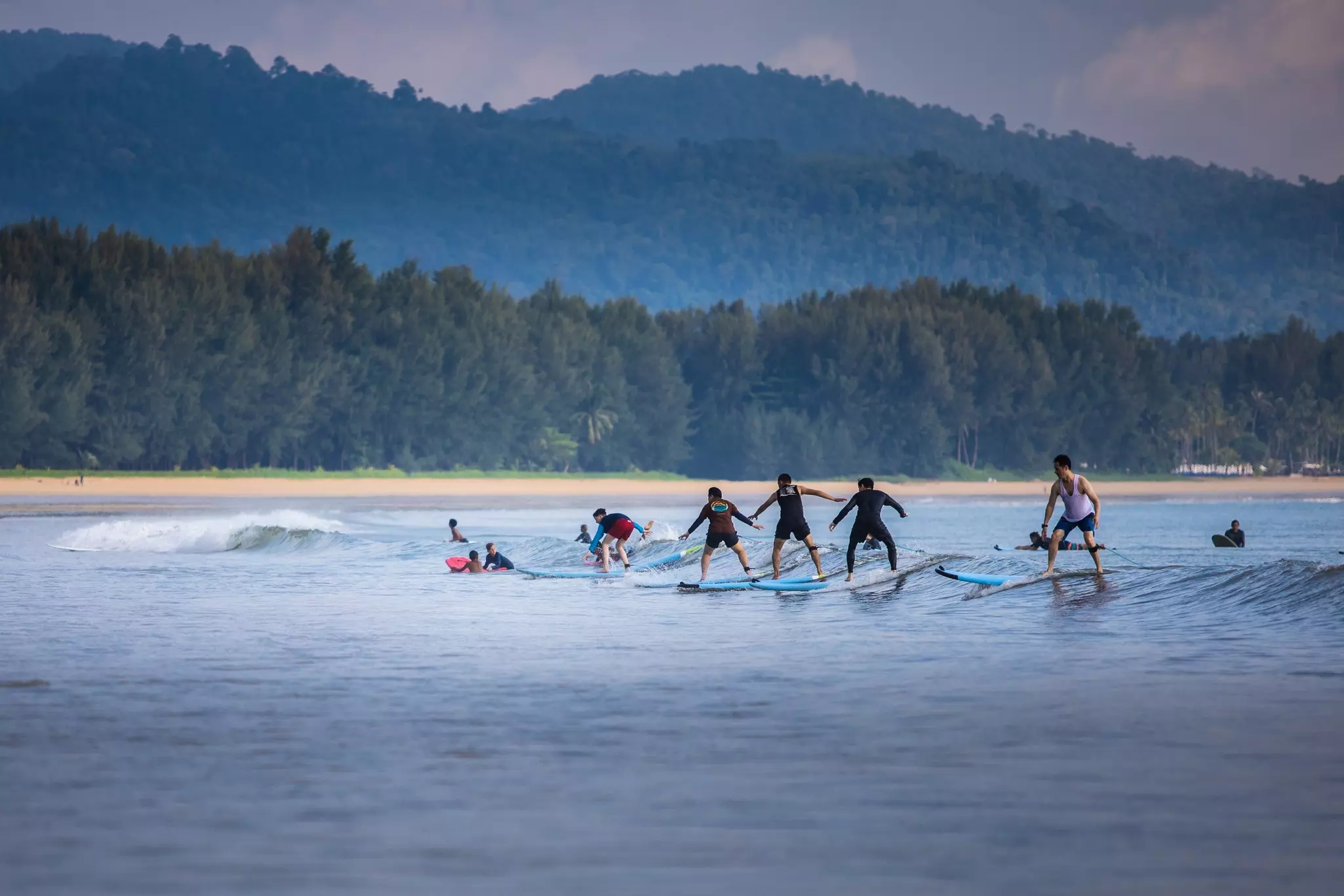 People learning to surf with lush green forestry as a backdrop