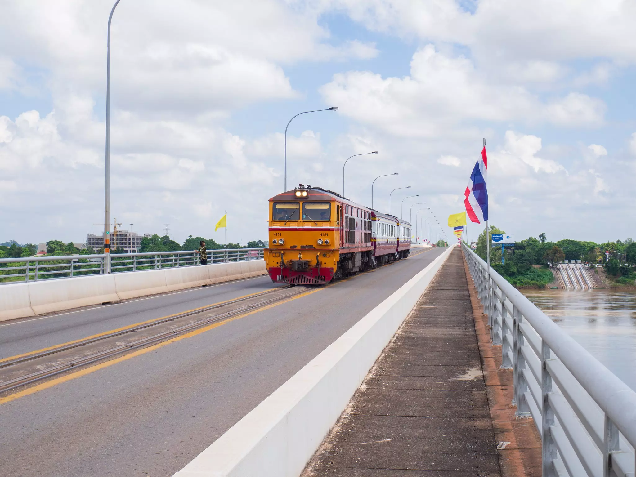 An orange train engine traverses a bridge over a river with a single track.