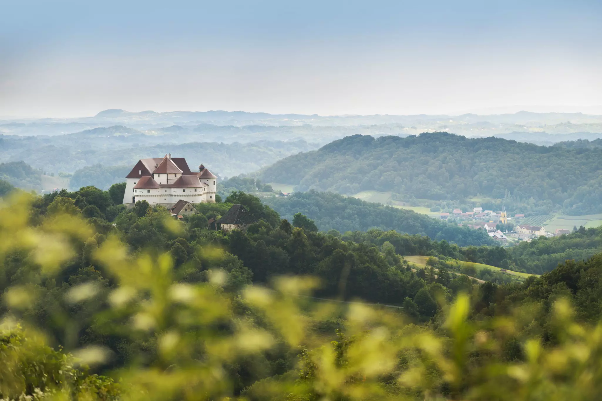 A multi-turreted castle peaks out from dense woodland in a rural area; Veliki Tabor near Zagorje, Croatia. 