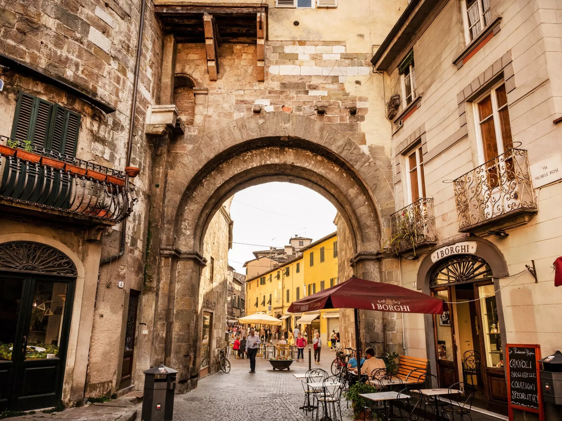 People walk through a large stone gate in a street in a historic city.