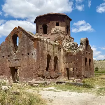 Roofless reddish stone church with an octagonal drum on open scrubland in Aksaray province, green hills and clouds behind