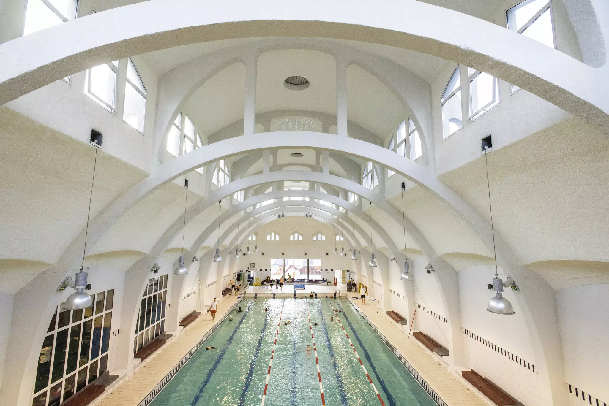 Swimmers in an indoor lap pool beneath white arched ceilings