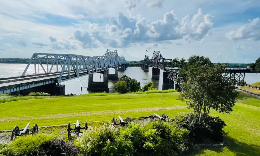 Two steel truss bridges span the wide Mississippi River at Vicksburg, with Civil War cannons on a lawn in front