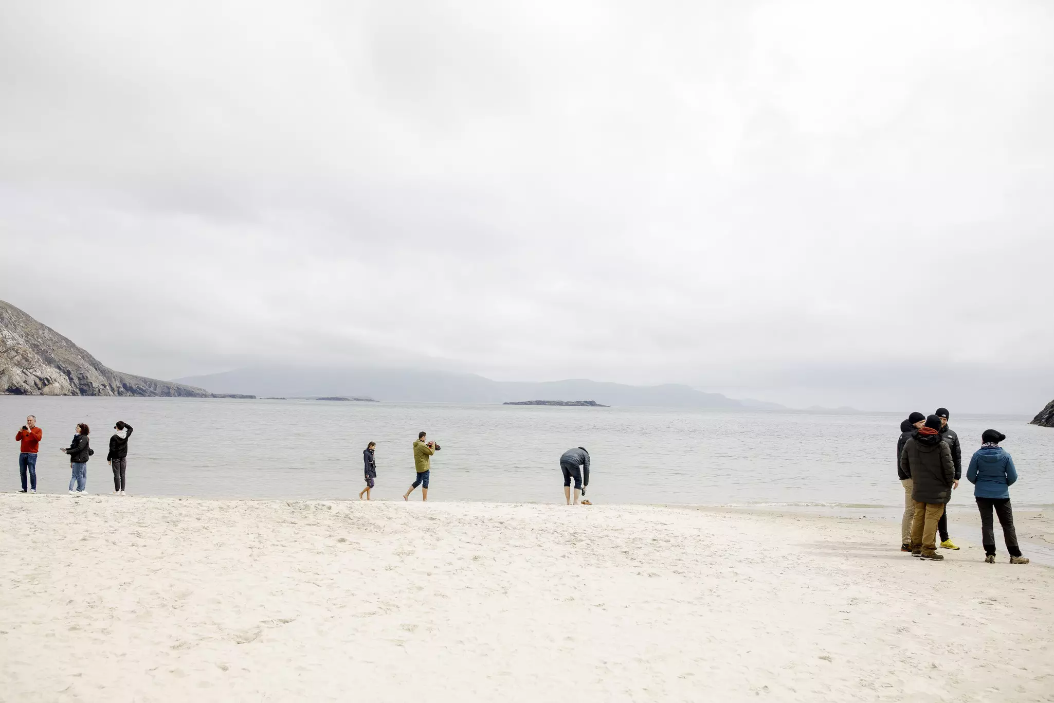 Visitors to a beach on an overcast day. Everyone is wearing a coat and most people have hats on too