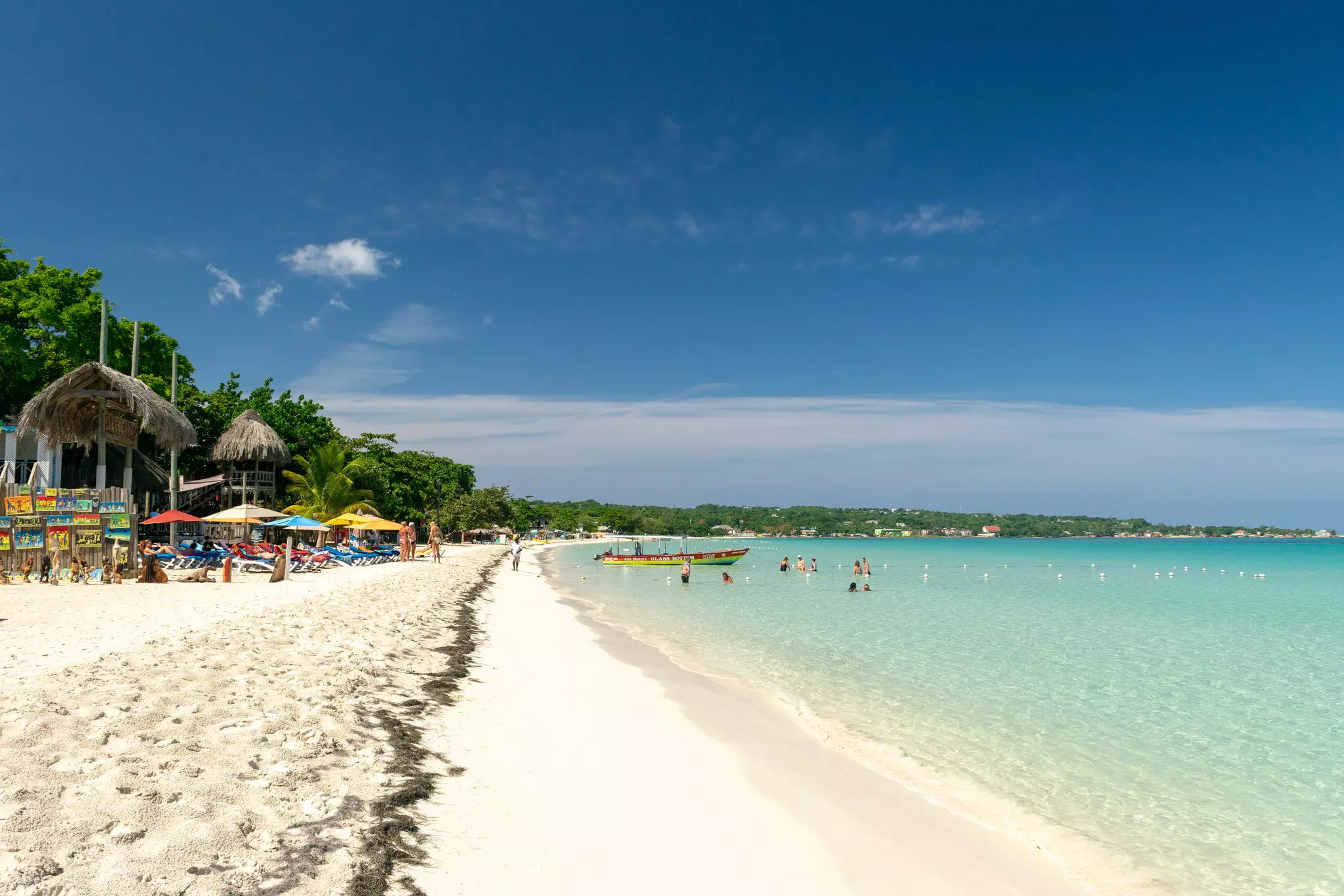 A white-sand beach stretching into the distance with some people swimming in the turquoise ocean