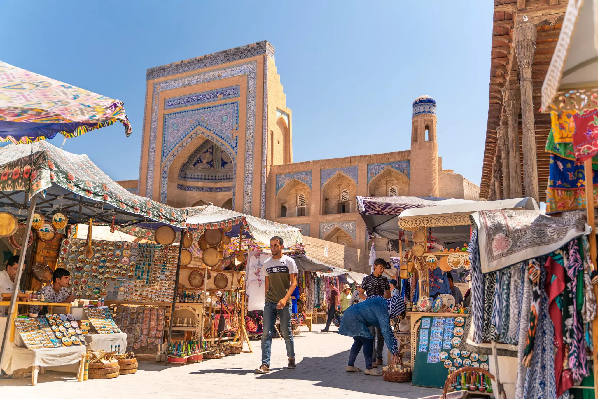 A bazaar in front of a blue-tiled medressa in the historic center of Khiva in Uzbekistan.