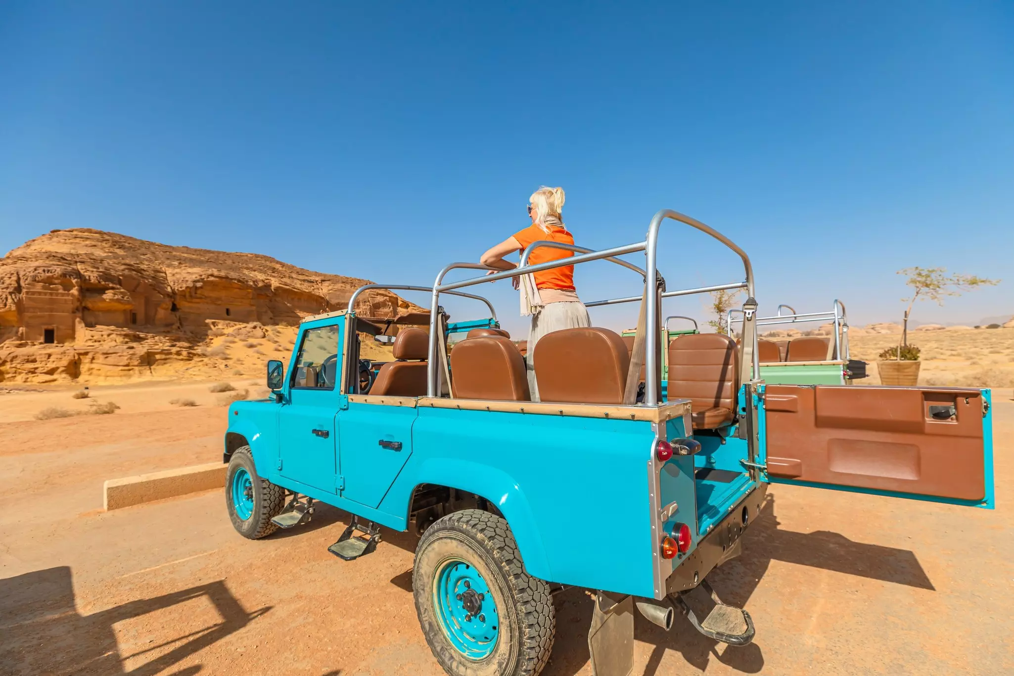 A person standing in a open blue Jeep looking at an archeological site carved into rock.
