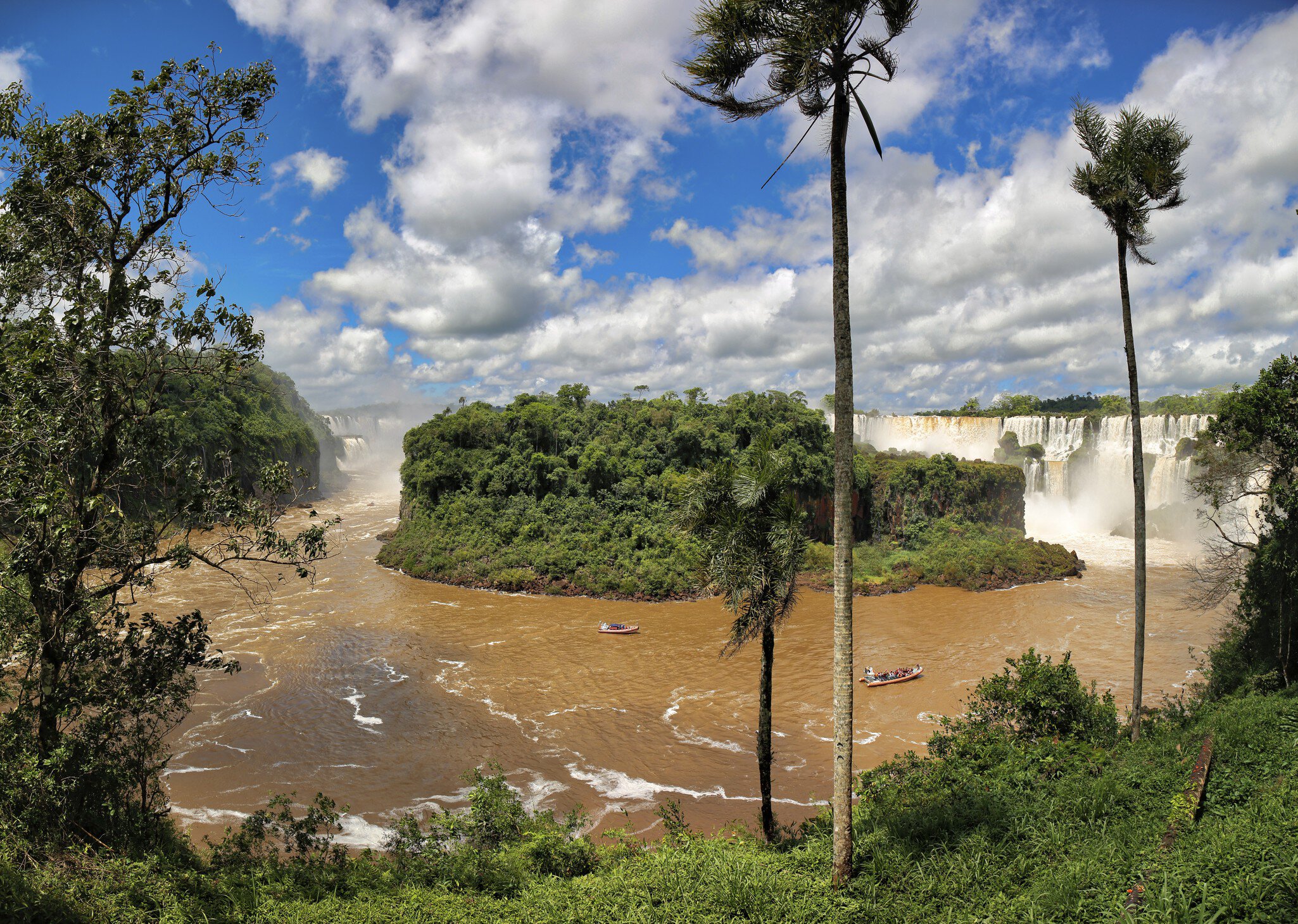 View to Isla San Martin with brown river and falls in background, blue sky and white clouds, Iguazu Falls, Argentina