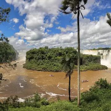View to Isla San Martin with brown river and falls in background, blue sky and white clouds, Iguazu Falls, Argentina