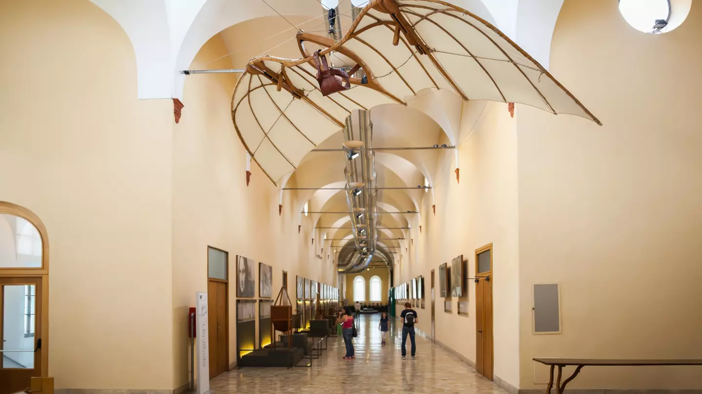 A corridor in a museum with displays on the walls. Above hangs a paraglider-like structure.