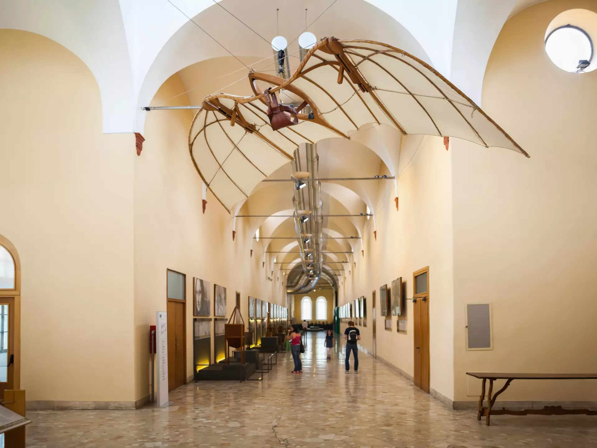 A corridor in a museum with displays on the walls. Above hangs a paraglider-like structure.