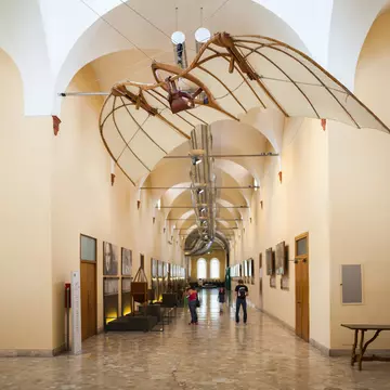 A corridor in a museum with displays on the walls. Above hangs a paraglider-like structure.