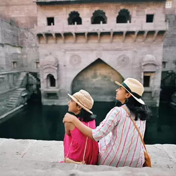 Rear view of a mother and daughter wearing hats and sitting at a step well (Toorji Ka Jhalra) in Jodhpur, Rajasthan, India.