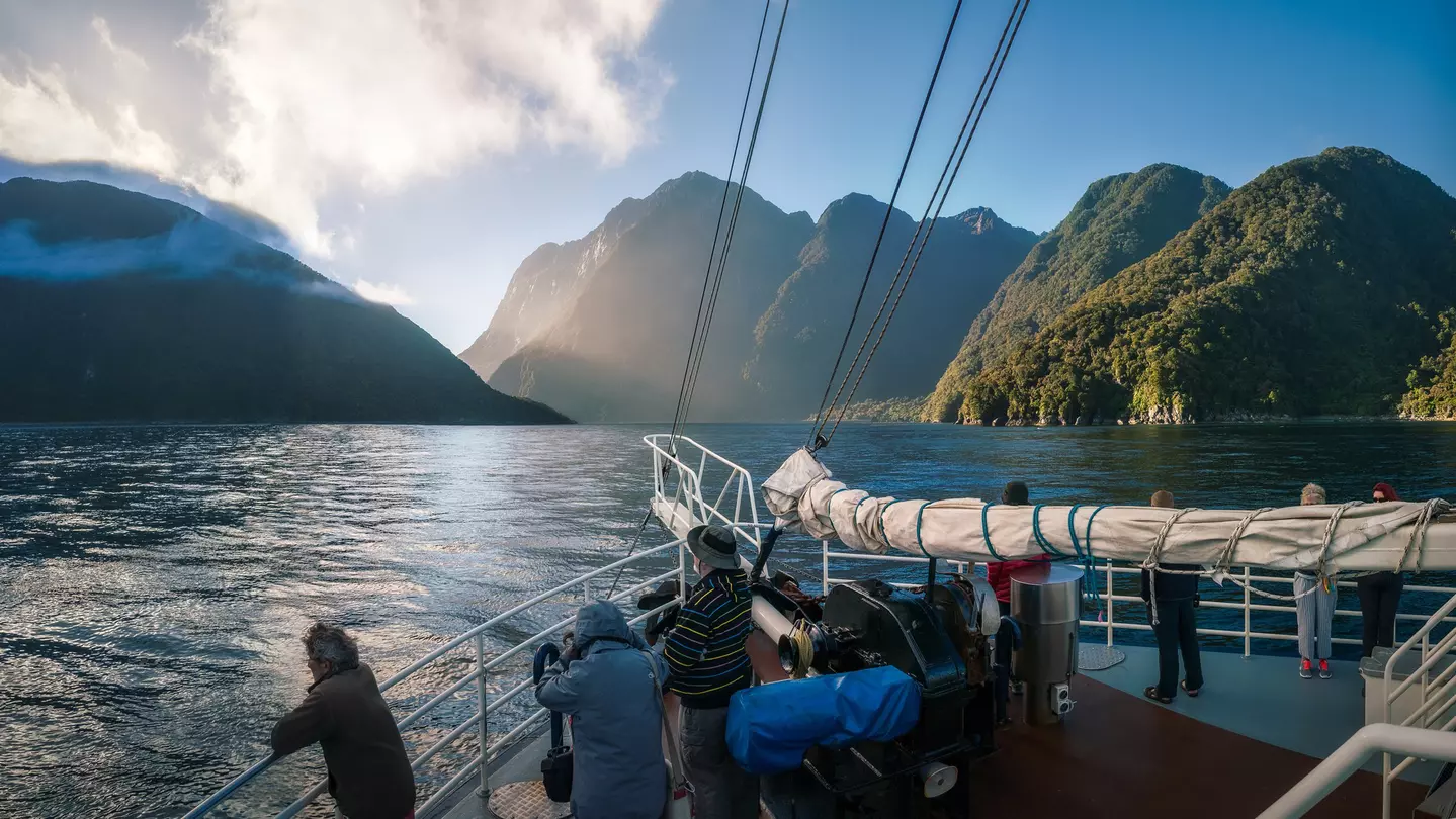People standing on the bow of a boat during an early morning cruise in Milford Sound, Fiordland National Park, New Zealand.