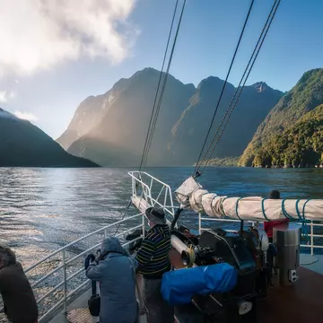 People standing on the bow of a boat during an early morning cruise in Milford Sound, Fiordland National Park, New Zealand.