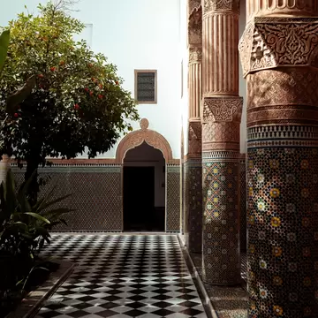 A courtyard with an orange tree, surrounded by intricate tile patterns and carvings on doors, walls, floors and columns.