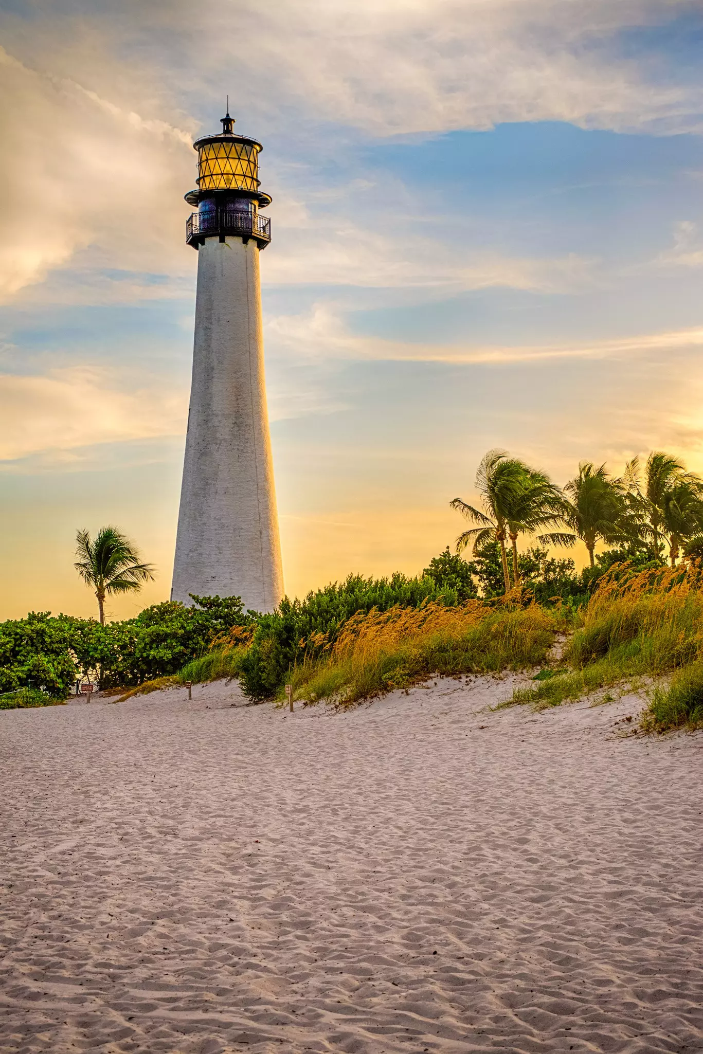 A large concrete lighthouse towers above grass-covered sand dunes.
