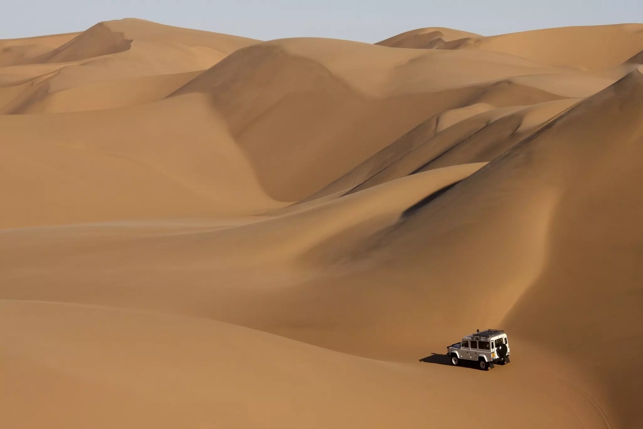 A four wheel drive travels through giant sand dunes in the Namib Desert. ©Steve Allen/Shutterstock