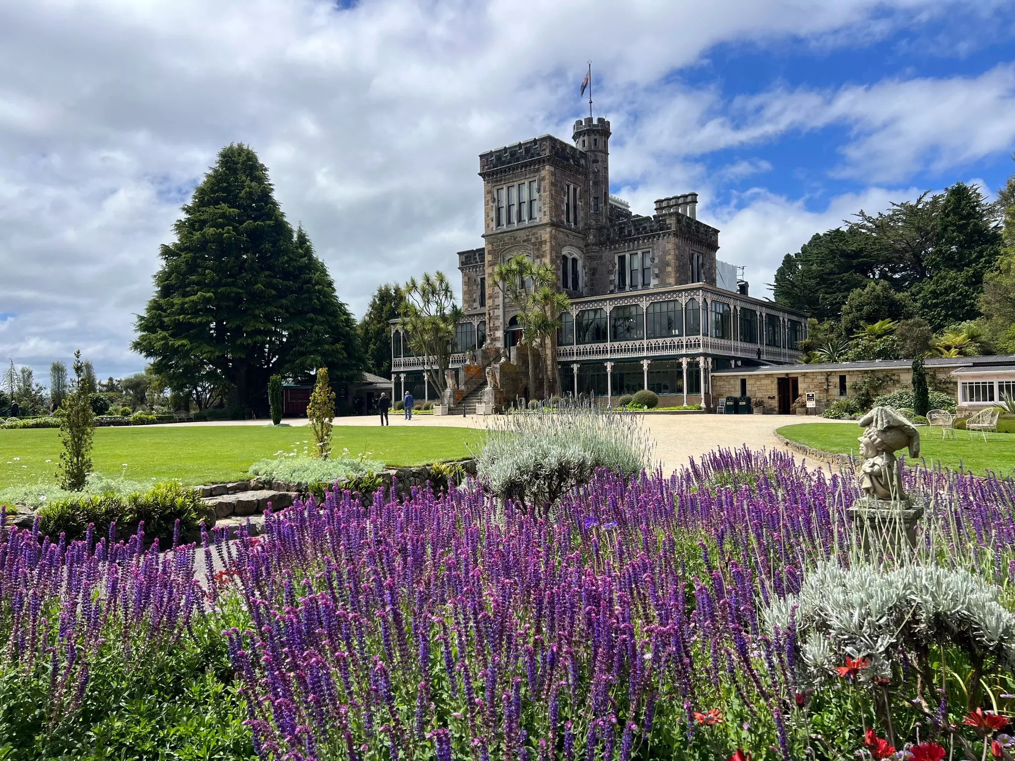 A grand stately home surrounded by beautiful gardens and purple flowers in bloom.