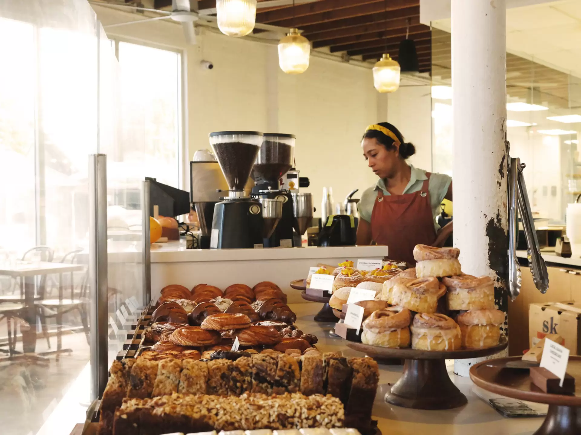 Assorted pastries on display at a bakery with a barista making coffee behind them