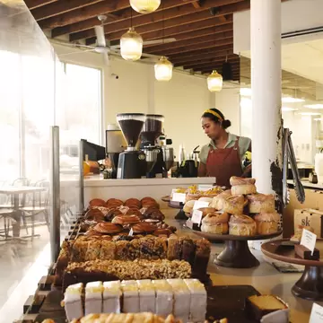 Assorted pastries on display at a bakery with a barista making coffee behind them