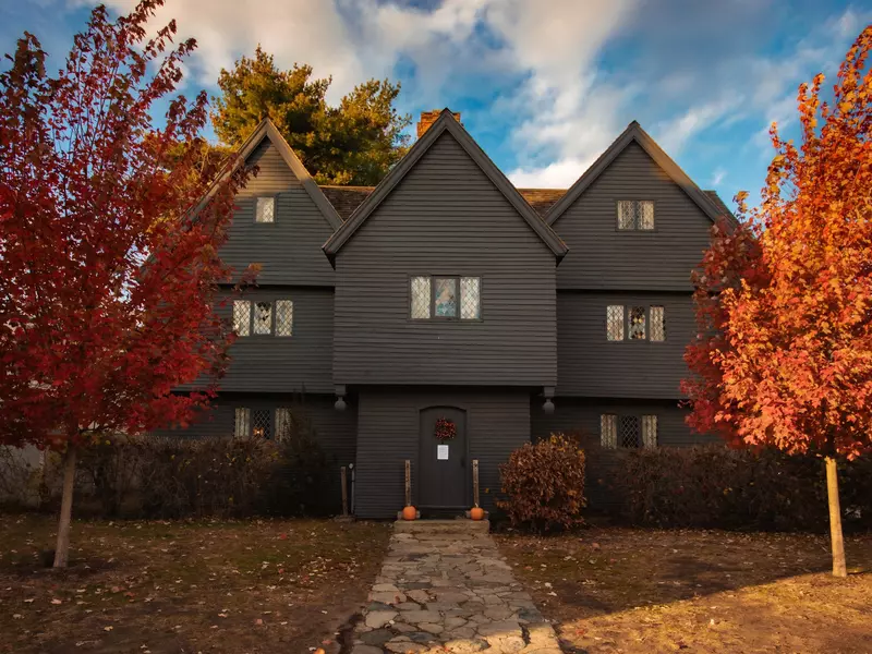 A large timbered house with small windows in fall with bright red trees out front.