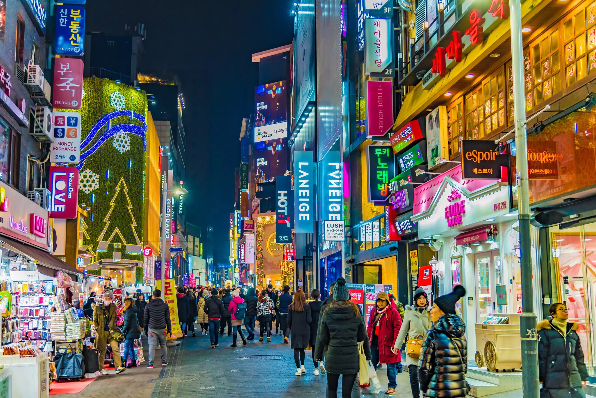 People walking on illuminated street amidst buildings at night in Seoul.