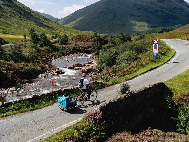 Charlie and family riding along a winding road beside a river in the Scottish Highlands.