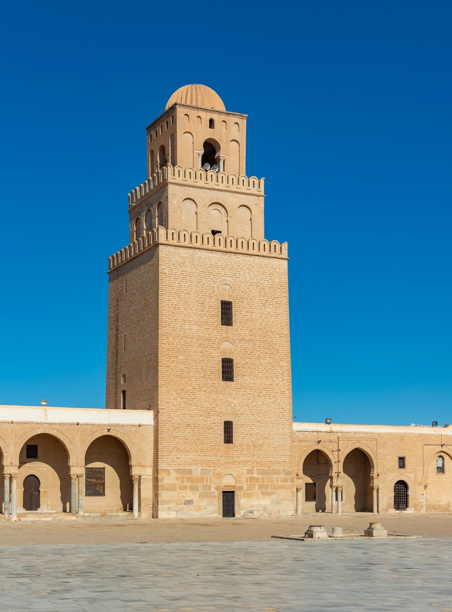 Three-tiered sandstone tower with crenellations and a ribbed dome rises above arcaded galleries and a paved courtyard