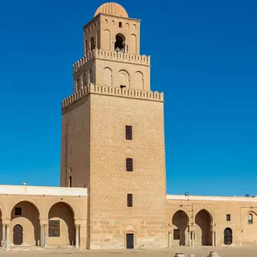 Three-tiered sandstone tower with crenellations and a ribbed dome rises above arcaded galleries and a paved courtyard
