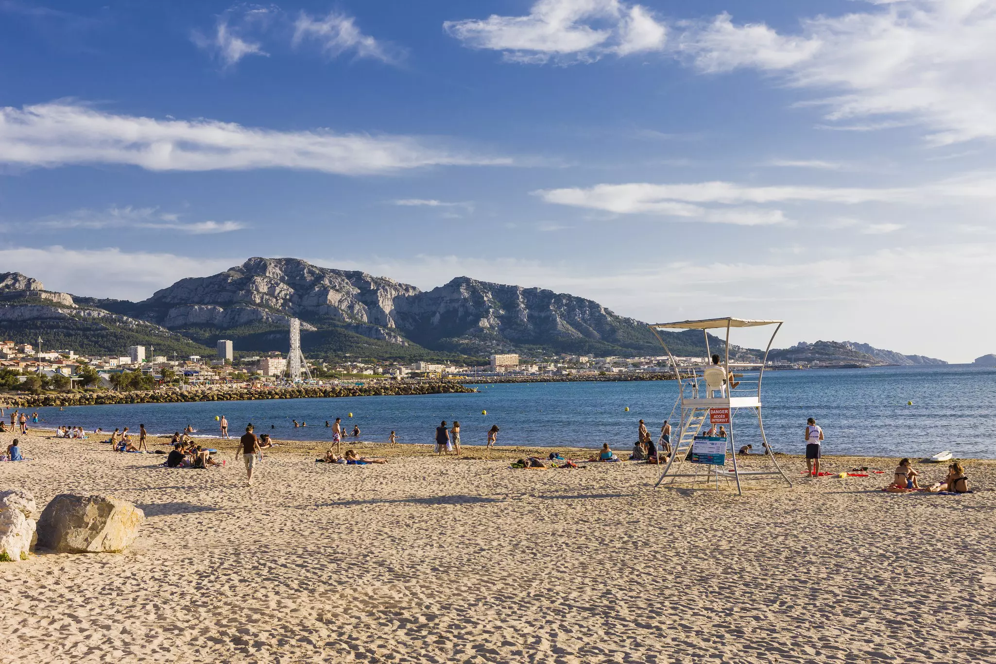 Beachgoers lie out at Prado Beach at Parc Balnéaire du Prado in Marseille, Bouches-du-Rhône, France, with rocky massifs seen in the distance