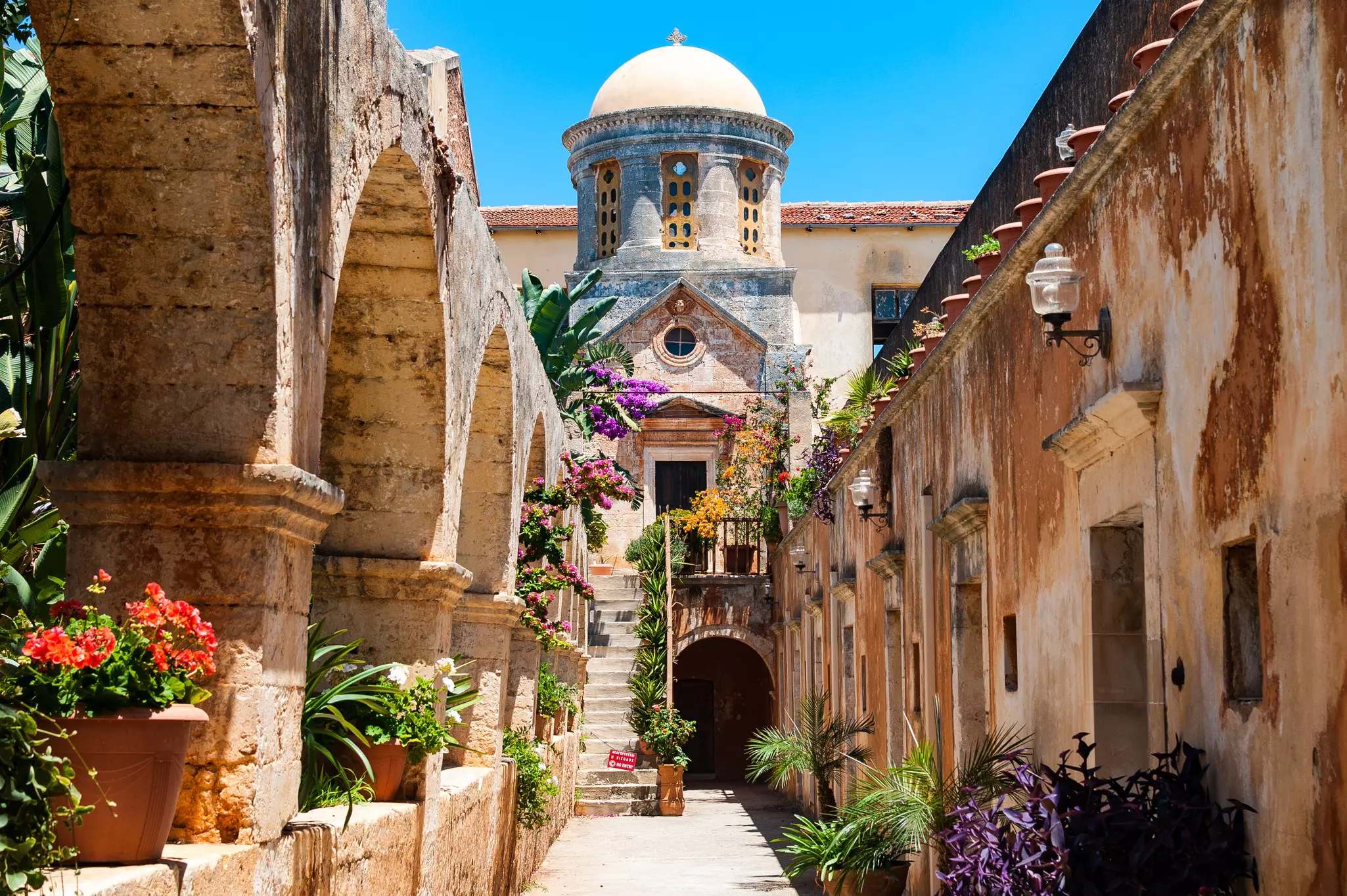 A flower pot-lined alleyway leads to a domed monastery.