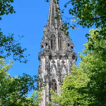 View of an ornate church tower through treetops on a sunny day.