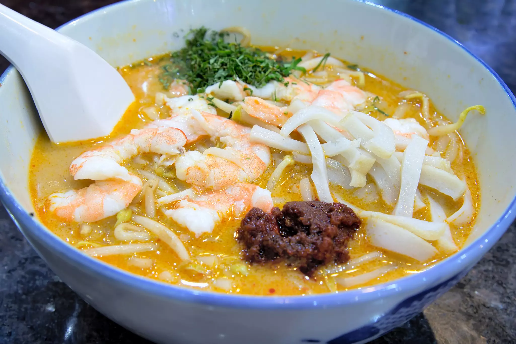 A close-up shot of a bowl of noodles with chili paste and shrimp in a yellow sauce.