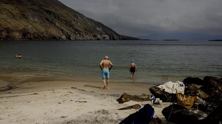 Bathers walk into a beach surrounded by a steep hill
