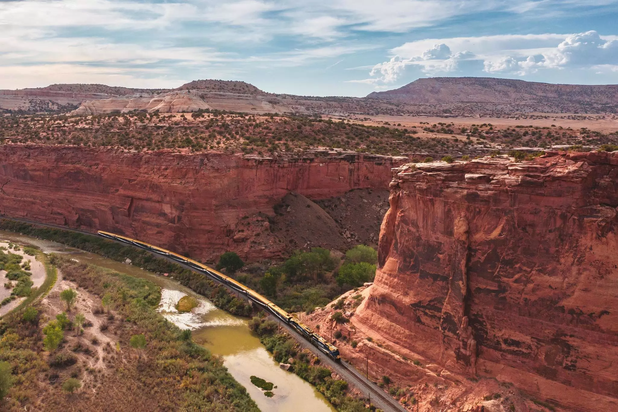 Aerial view of a train traveling in a canyon below red steppe mountains.