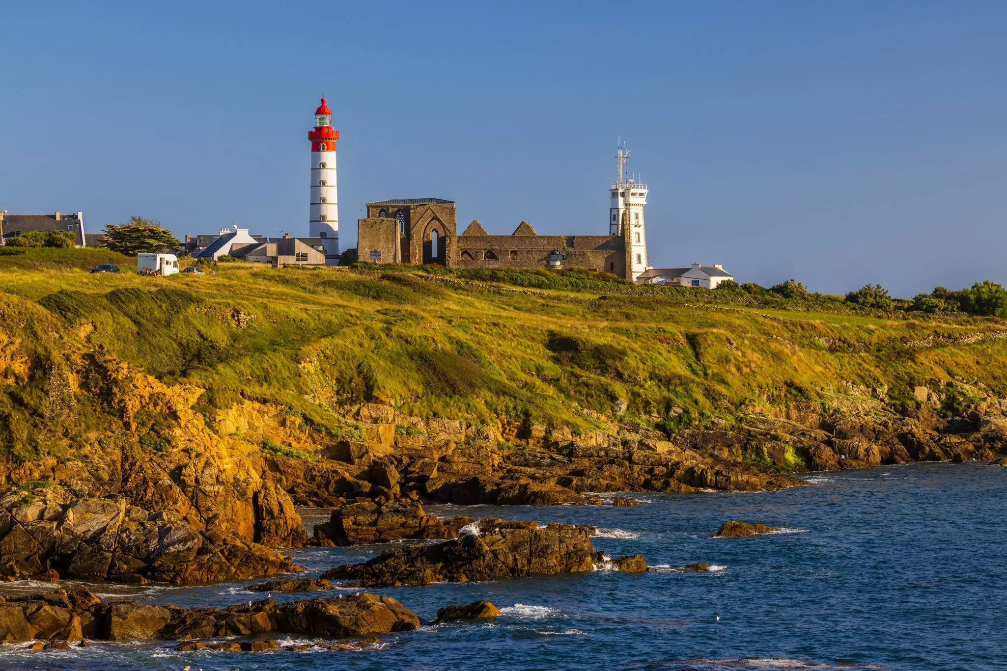 A red-and-white lighthouse at the end of a grassy lawn, with a stone structure below it.