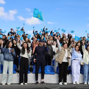 Groups of spectators cheer and wave Kazakhstan's blue and yellow national flag on the side of the game arena at the World Nomad Games in 2024 
