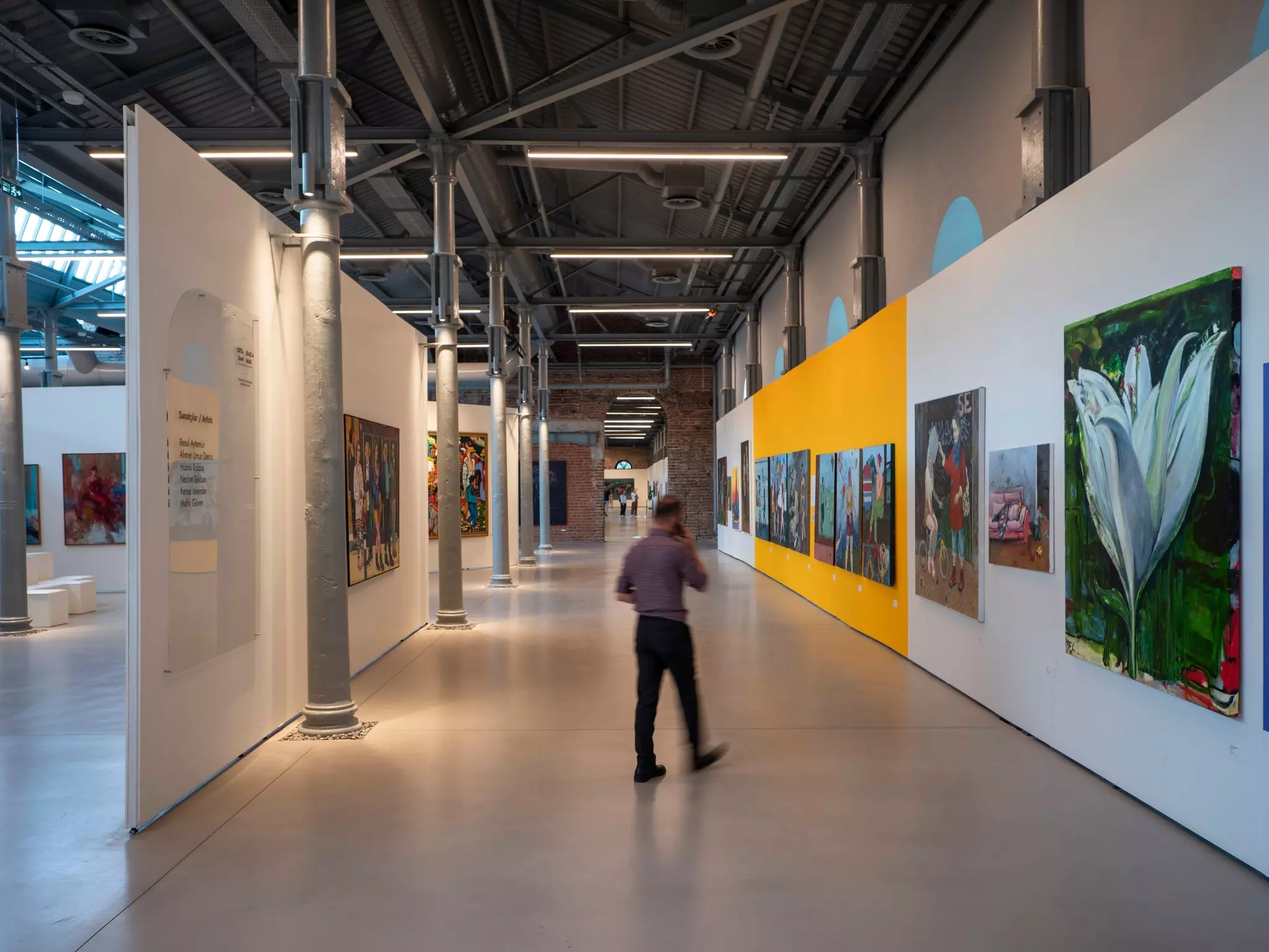 A man walks through a gallery with large paintings hanging on the walls.
