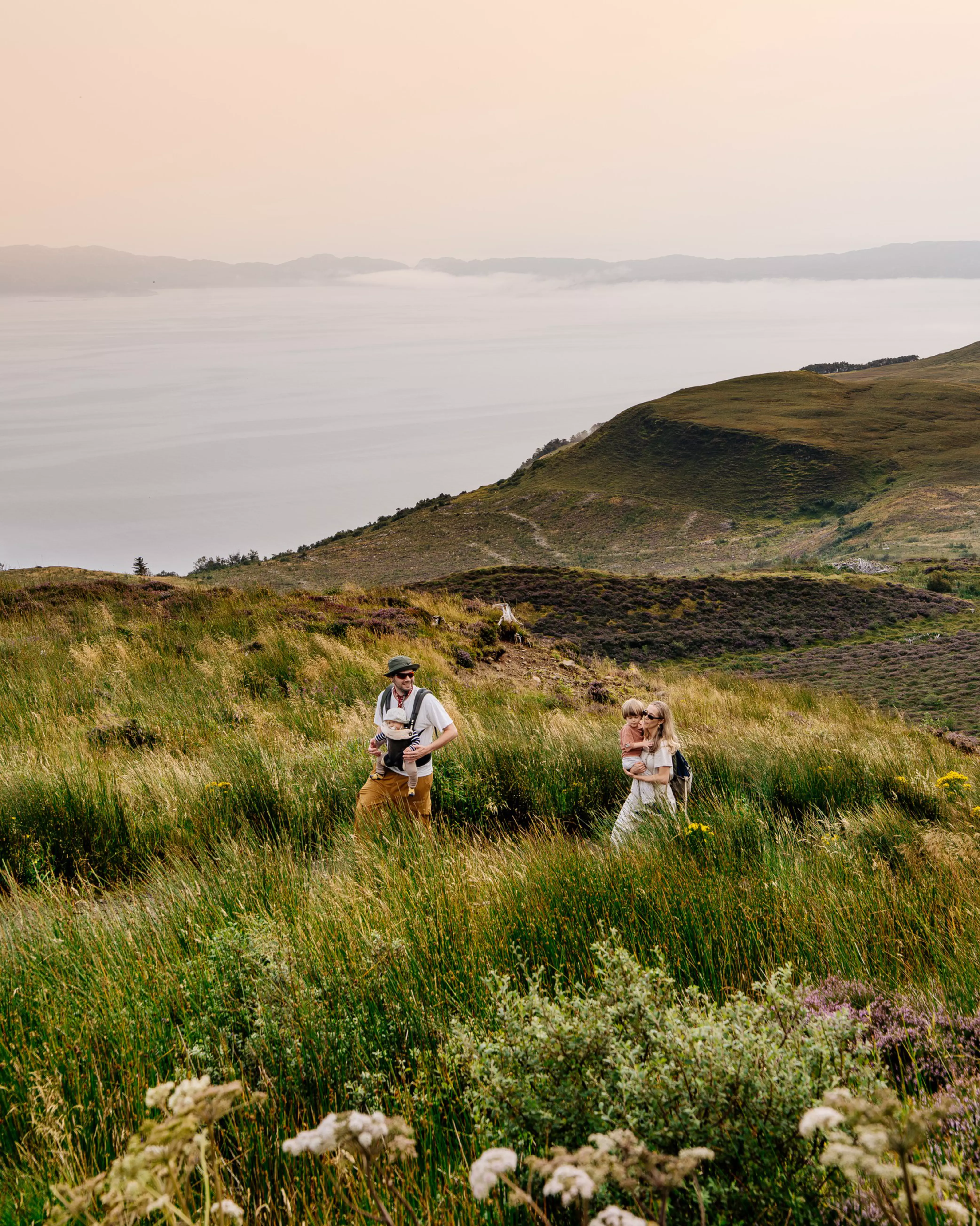 Charlie and Jessica Last walking with their children through tall grass in the Scottish Highlands.