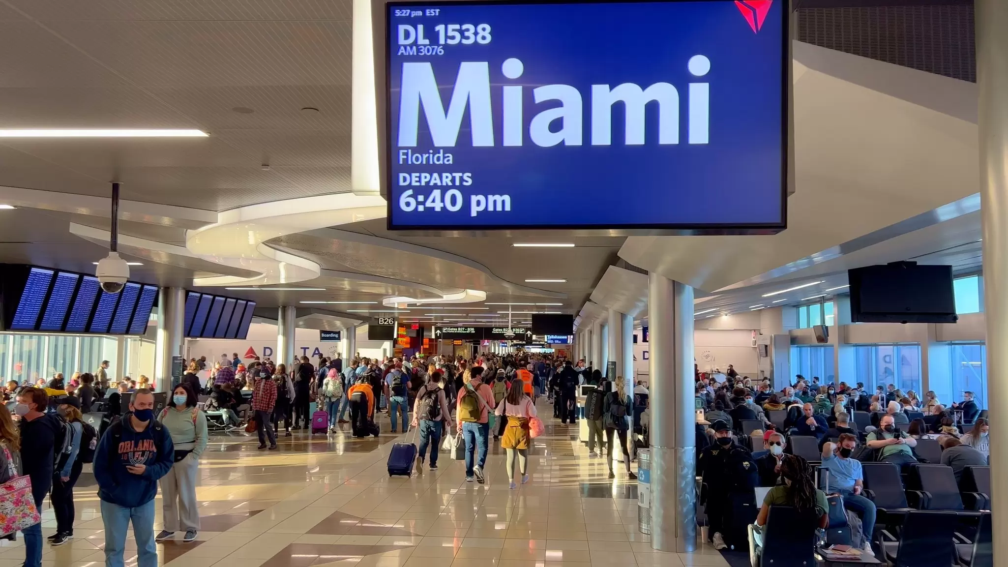A busy airport terminal (Atlanta Airport) with a sign indicating the flight at the departure gate is going to Miami.
