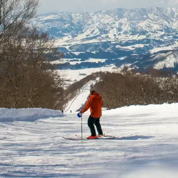 A skiier on a snow-covered slope at Nozawa Onsen in Japan looks towards the distant mountains