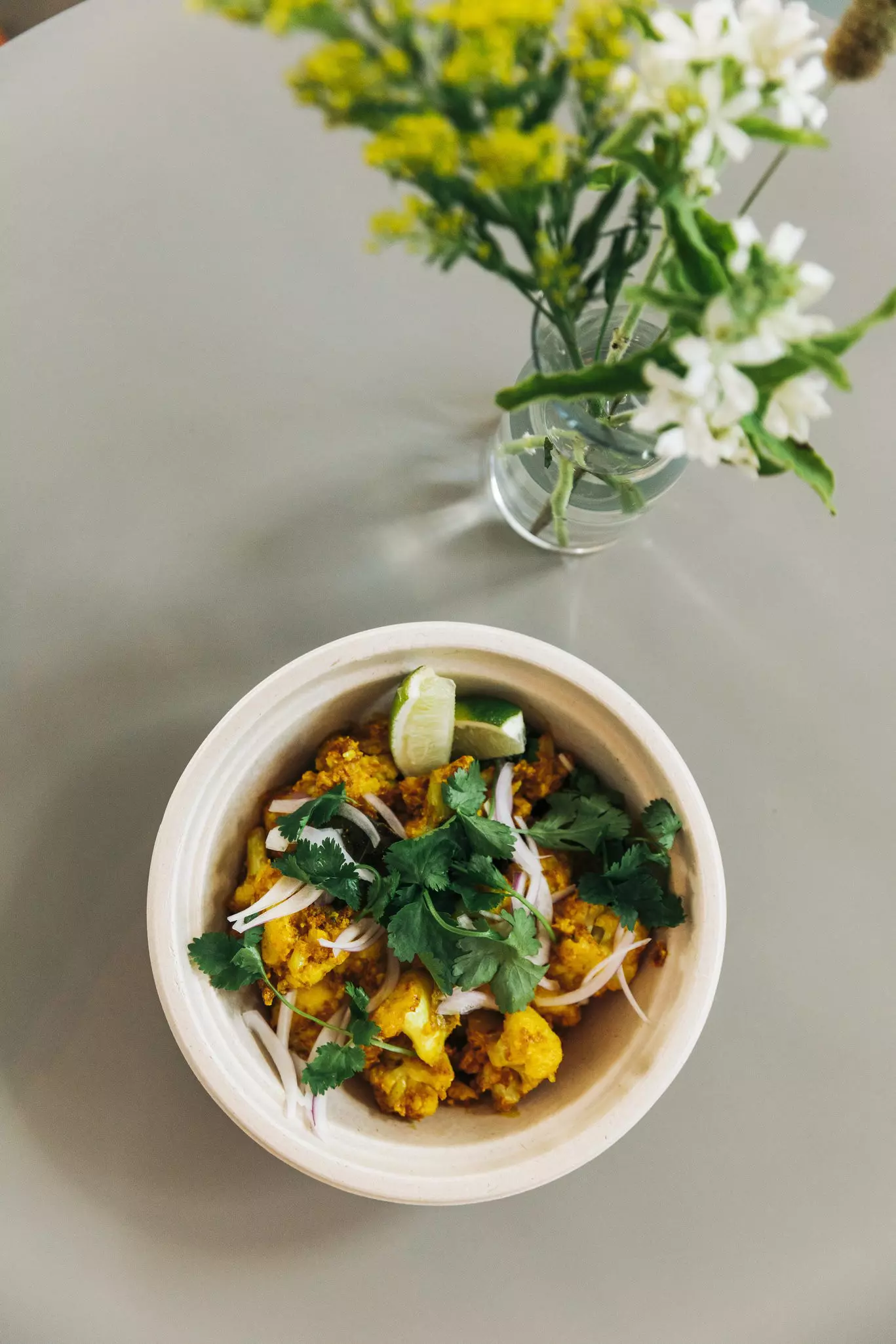 A dish of fried spiced cauliflower with an onion and cilantro garnish