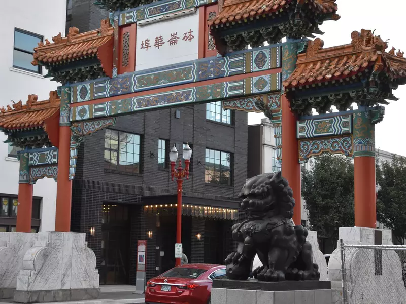 A Chinatown Gateway with a car driving through it in an urban setting.