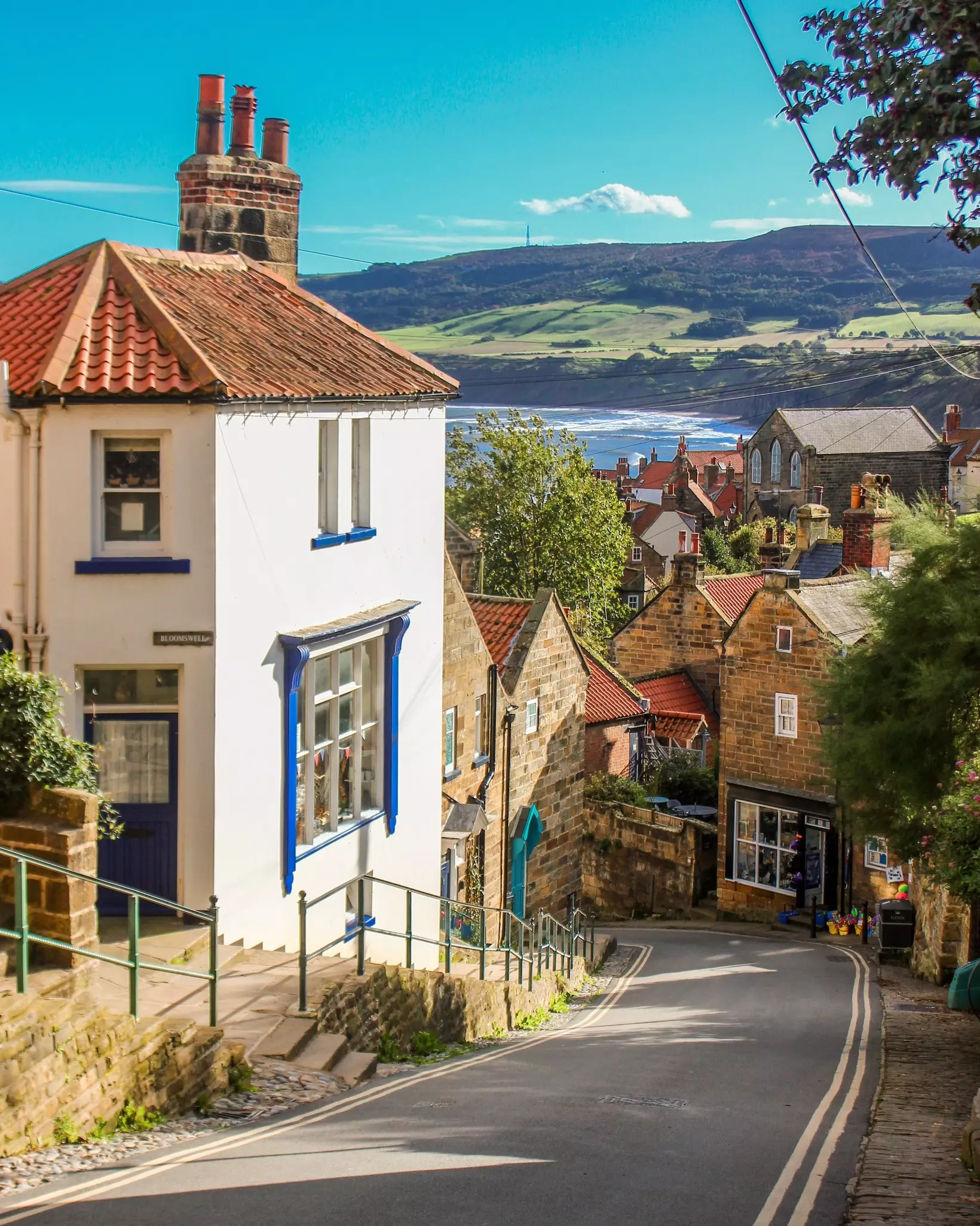 A narrow street leads down through a coastal village. Waves lap on the shallows at the foot of high hills.