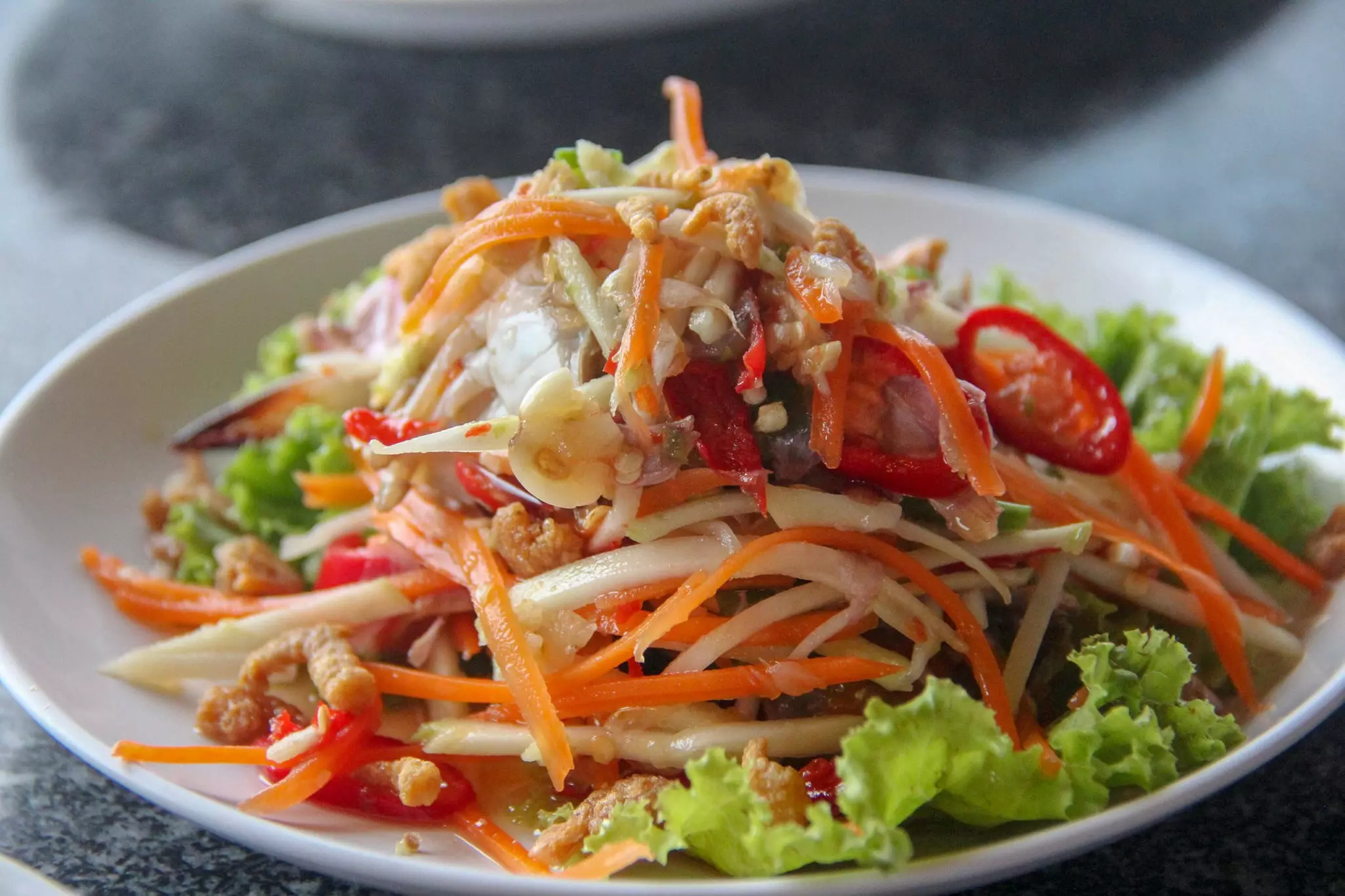 Spicy green papaya salad (Som Tam) mixed with vegetables, fresh blue crab and Thai herbs.