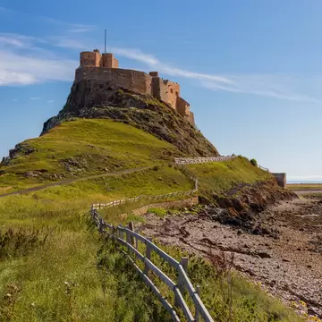 Green meadows and a rocky shore by the castle on the holy island of Lindisfarne, Northumberland, UK. 