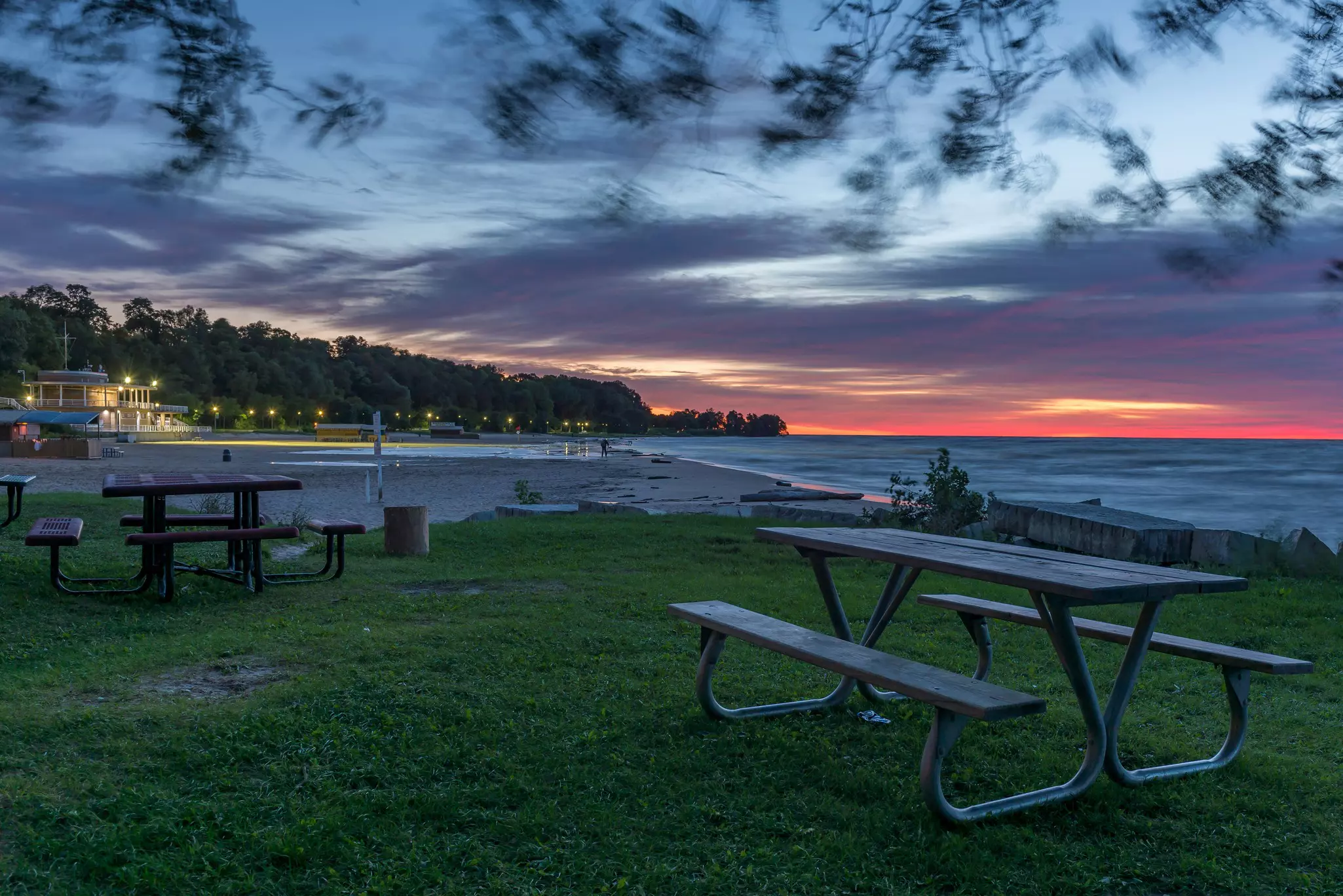Sunrise at a lakeside beach with picnic tables on a grassy area in the foreground.
